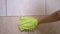 Female Hand Wipes Bathroom Tiles in Circular Motion with Green Microfiber Mitt