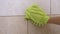 Female Hand Wipes Bathroom Tiles in Circular Motion with Green Microfiber Mitt