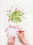 Female hand Write a greeting card on white wooden background with flowers bunch and pink ribbon, top view, copy space