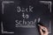 Female hand writes the phrase Back to school with white chalk on black chalkboard.