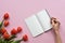 Female hand writing on a notebook. Pink background with tulips. Copy space.