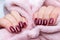 Female hands with beautiful manicure - dark red glittered nails with pink fluffy fabric, textile. Selective focus