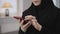 Female hands with beautiful manicure scrolling on smartphone. Young unrecognisable muslim woman in black hijab using