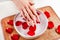 Female hands with beige nails natural color and bowl with water and red rose petal