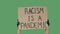 Female hands in black gloves pick up a poster from a cardboard box that reads RACISM IS A PANDEMIC. Struggle for