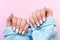 Female hands in blue knitted sweater with beautiful manicure - white ivory nails with flower on pink paper background