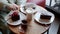 Female hands breaking off cake piece with fork on table in cafe top view. Two woman drinking tea and eating chocolate