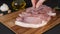 Female hands of a chef decorate with coarse salt, pepper and rosemary fresh pieces of pork bacon meat on a wooden