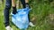 Female hands collecting plactic trash in the blue package. Nature cleaning, ecology volunteer, green concept.