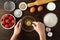 Female hands cooking strawberry cake or pie on dark wooden table.