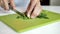 Female hands cut greens with metal knife on bright green cutting board, close-up