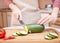 Female hands cut with a knife a young seasonal zucchini into slices on a wooden cutting board. The method of preparation of