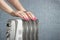 Female hands on electric oil radiator close-up on blue background