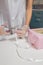 Female hands in gloves cutting with scissors white ribbon to decorate pink box of cupcakes on white table background. Mothers day