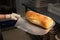 Female hands in gloves hold a shovel with a loaf of artisan bread. Homemade bread production