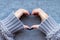 Female hands in gray knitted sweater with beautiful manicure - dark gray blue glittered nails making heart symbol on knitted