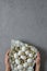 Female hands hold chicken and quail eggs in a plate with a towel on a gray concrete background. Top view. Flat lay