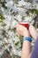 Female hands hold a cup of coffee with flowering cherry tree on the background