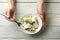 Female hands hold fork and bowl with feta cheese on white wooden background