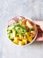 Female hands hold Hawaiian Shrimp Poke Bowl with Vegetables, mango and Rice on a gray background. top view