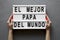 Female hands hold lightbox with `El Mejor Papa Del Mundo` words over concrete background. Overhead, from above, flat lay. Father