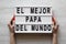 Female hands hold lightbox with `El Mejor Papa Del Mundo` words over white wooden background. Overhead, from above, flat lay.