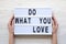 Female hands hold modern board with `Do what you love` word on lightbox over white wooden background, from above