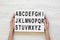 Female hands hold modern board with english alphabet on lightbox over white wooden background, from above.