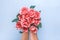 Female hands hold romantic bouquet of tender pink roses on pastel blue background