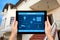Female hands hold a tablet with system smart house on the background of the house