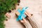 Female hands hold wrapping christmas gift box with blue ribbon on brown wooden table. Top view