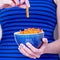 Female hands holding bowl with orange lentil fusilli pasta on a blue striped background. Diet and gluten free concept