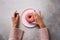 Female hands holding donut on pink plate over stone background. Top view, flat lay. Sweet, dessert, diet concept. Weight lost