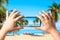 Female hands holding mobile smart phone and making photo of amazing beach with palms and ocean. Vacation and relaxation concept