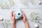 Female hands holding modern polaroid camera on a blue wooden background with flowers. Top view, tender minimal flat lay style comp