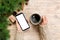 Female hands holding modern smartphone with mosk up and mug of coffee on wooden table with christmas decoration. top view