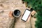 Female hands holding modern smartphone with mosk up and mug of coffee on wooden vintage table with christmas decoration. top view