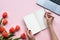 Female hands holding  notebook. Pink background with laptop and tulips. Copy space.