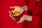 Female hands holding Potato chips with chili peppers on red background. spicy food, unrecognizable person