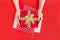 Female hands holding red goft box present with golden bow on red background. Festive backdrop for holidays: Birthday