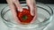Female hands holding a ripe tomato in a bowl of water, Slow motion. Woman chef washing one red tomato with a green stem