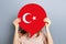 Female hands holding a round information piece of paper dialog with turkish flag emblem isolated over grey studio