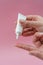 Female hands holding and squeezing tube of cream gel on pink background. Ð¡osmetic bottles for beauty or medicine products