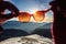 Female hands holding sunglasses through which you can see a beautiful inter sunset in the mountains of blue and orange