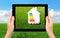 female hands holding a tablet with a house and sign energy saving on a background of field