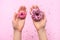 Female hands holding two donuts. Pink background