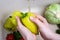 Female hands holding two fresh green sweet pepper under running water from the tap over the kitchen sink in where you can find