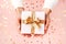 Female hands holding white gift box tied with gold ribbon confetti on pink background. Holiday presents shopping celebration