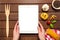 Female hands holding a white tablet with copy space on a wooden background with ingredients for cooking Italian pasta, top view