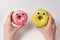 Female hands holding yellow and pink donuts with huge eyes and cheerful face on white background